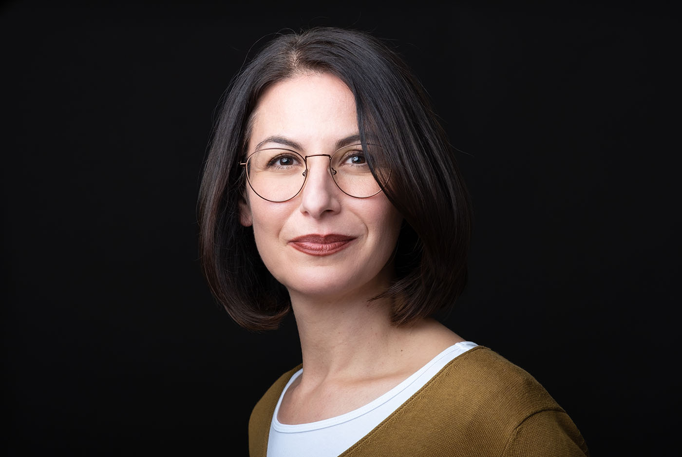 Bewerbungsfoto einer Frau mit buntem Pullover und Brille vor schwarzem Hintergrund, aufgenommen im Fotostudio KARRIEREPORTRAITS in Dortmund