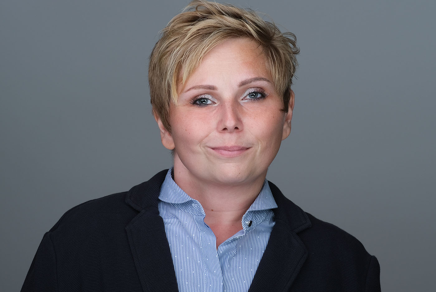 Bewerbungsfoto einer Frau mit hellblauer Bluse und dunkelblauem Sakko vor grauem Hintergrund, aufgenommen im Fotostudio KARRIEREPORTRAITS in Dortmund