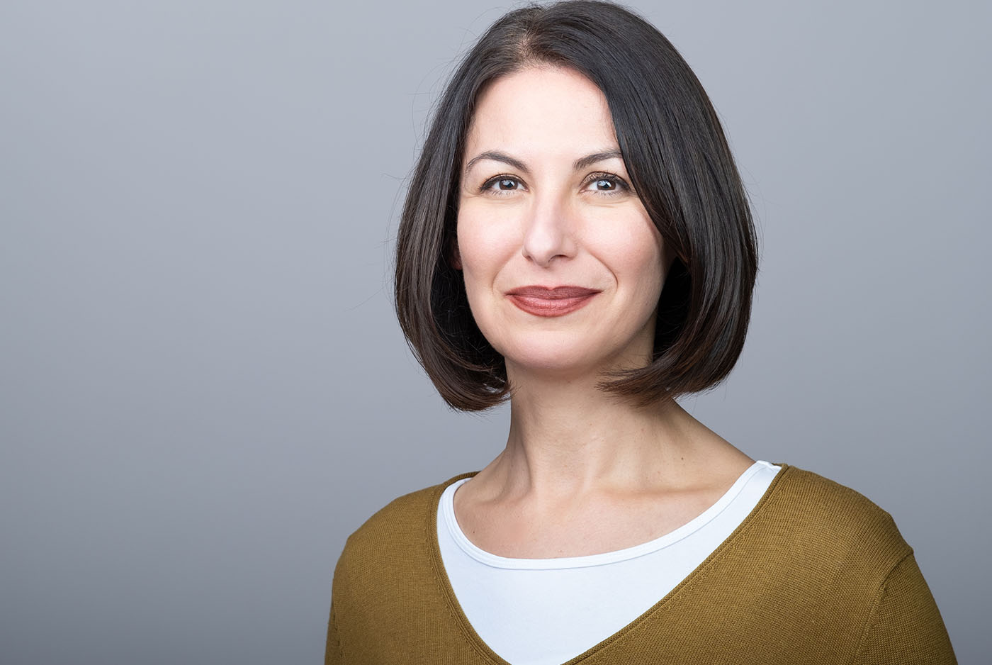 Bewerbungsfoto einer Frau mit buntem Pullover vor grauem Hintergrund, aufgenommen im Fotostudio KARRIEREPORTRAITS in Dortmund