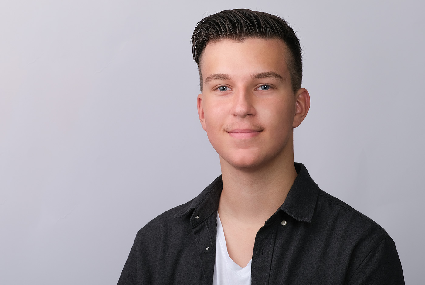 Bewerbungsfoto eines männlichen Teenagers mit weißem T-Shirt auf hellgrauem Hintergrund, aufgenommen im Fotostudio KARRIEREPORTRAITS in Dortmund