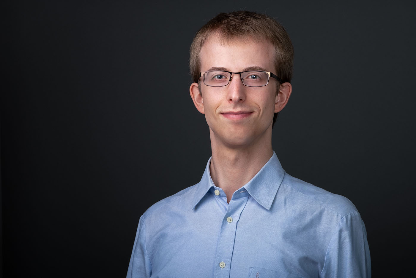 Bewerbungsfoto eines jungen Mannes mit hellblauem Hemd vor dunkelgrauem Hintergrund, aufgenommen im Fotostudio KARRIEREPORTRAITS in Dortmund