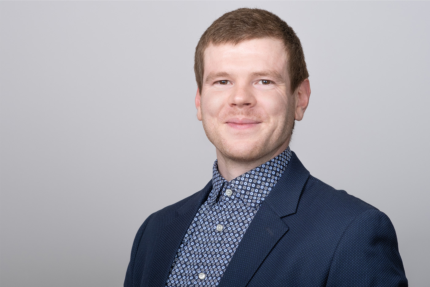 Bewerbungsfoto eines jungen Mannes in gemustertem hemd mit dunkelblauem Sakko auf hellgrauem Hintergrund, aufgenommen im Fotostudio KARRIEREPORTRAITS in Dortmund