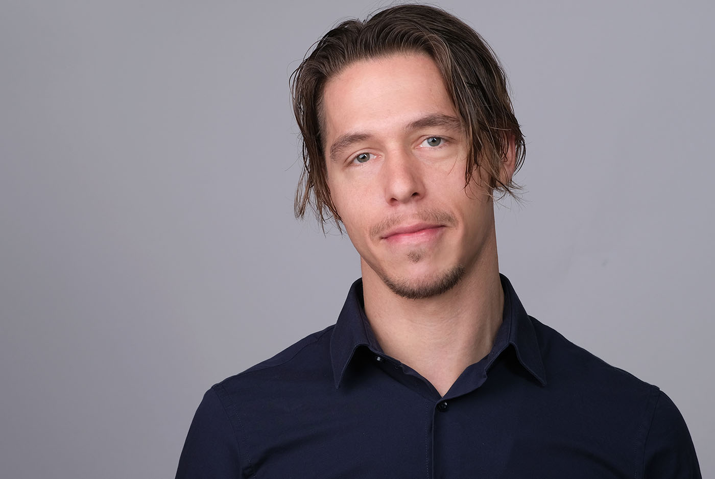 Bewerbungsfoto eines jungen Mannes mit dunkelblauem Hemd vor grauem Hintergrund, aufgenommen im Fotostudio KARRIEREPORTRAITS in Dortmund